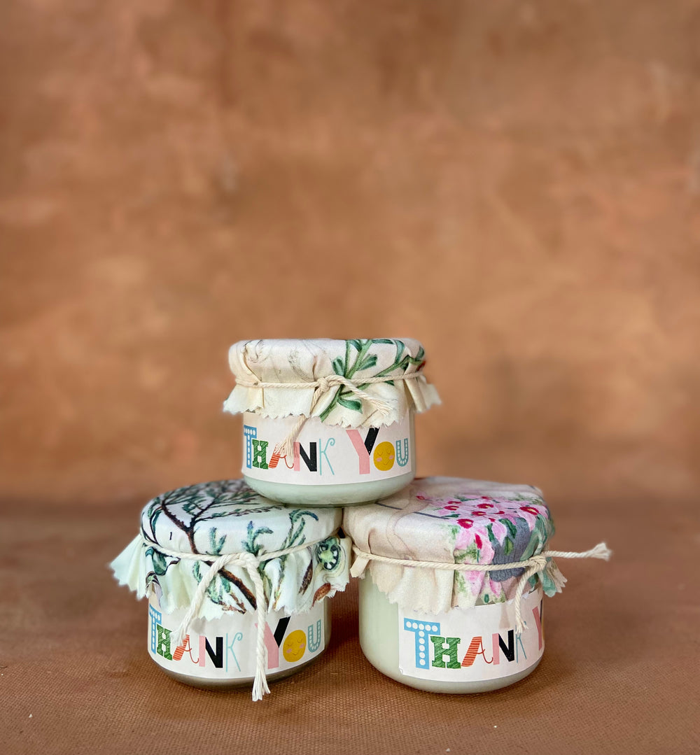 A stack of three candle pots with floral material lids, a label reading 