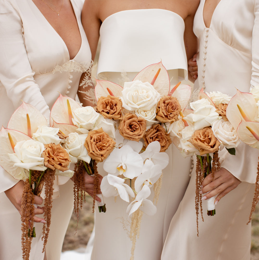 Bride and bridesmaids in white dresses holding beautiful, delicate bouquets of calla lilies, roses and orchids.