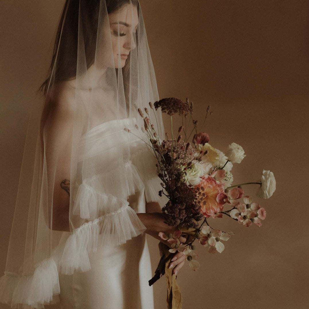 Dream photograph of a young bride wearing a gauze veil holding a structured bouquet of delicate blooms