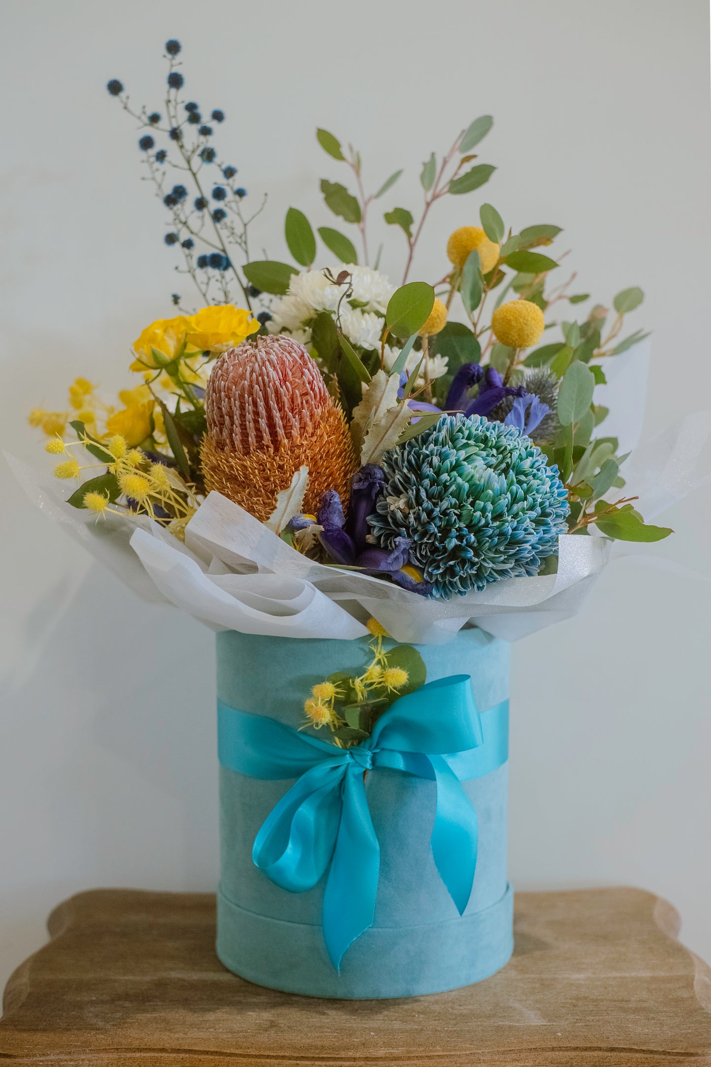 Photograph of a bright blue hatbox with colourful native flowers 