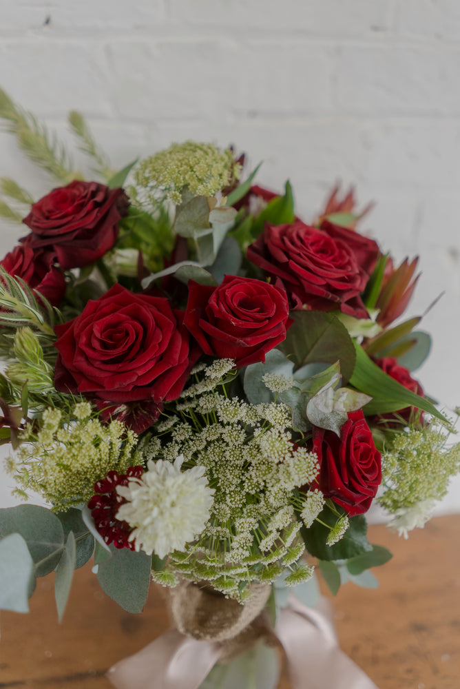 
                  
                    Close up of beautiful arrangement featuring Tasmanian red roses with elegant green and white florals in a tall glass vase
                  
                