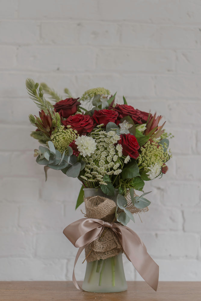 Beautiful arrangement featuring Tasmanian red roses with elegant green and white florals in a tall glass vase