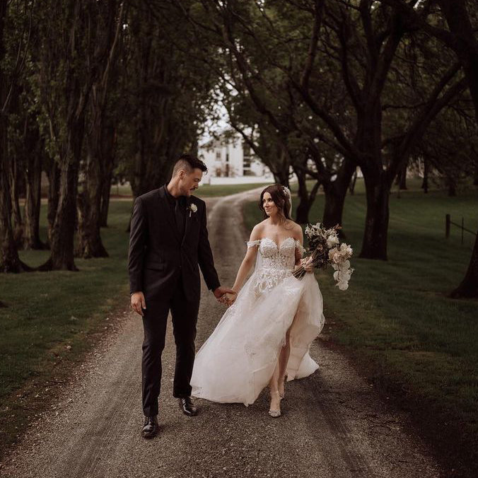 Photograph of a bride and groom walking down a tree-lined path