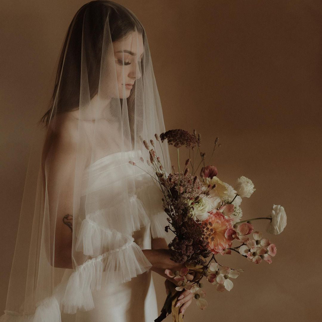 Dream photograph of a young bride wearing a gauze veil holding a structured bouquet of delicate blooms